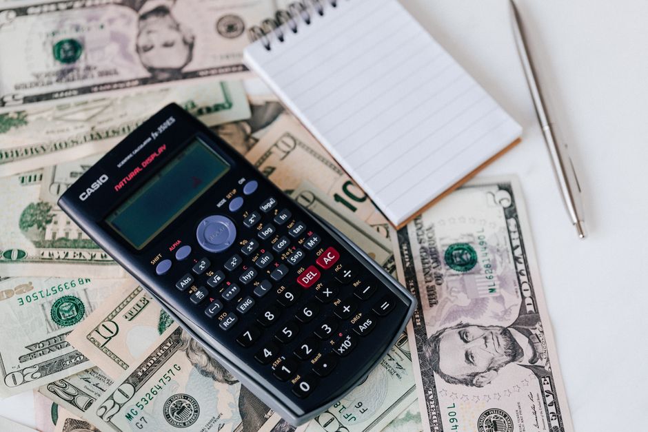 Average cost of pet insurance per month review: a calculator and notepad placed on a stack of U.S. dollar bills on a clean desk, the kind of household budget exercise where comparing the average cost of pet insurance per month against expected veterinary spending drives the structural decision on whether and how much to insure