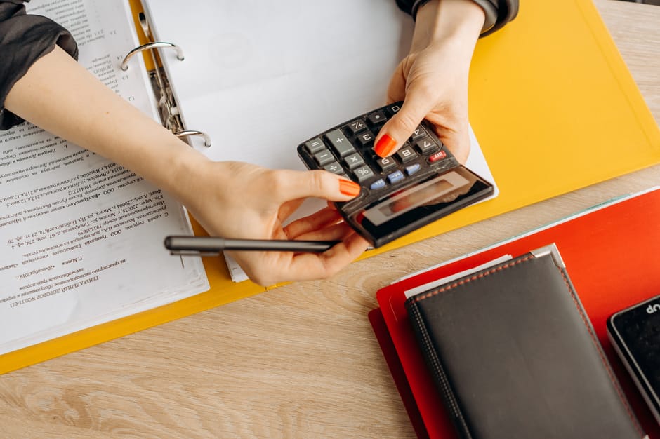 Pet insurance deductible explained at the kitchen table: a calm pet owner reviewing a policy document and using a calculator alongside a notepad, the kind of careful side-by-side review where pet insurance deductible explained correctly turns into a confident household enrollment decision before any policy is signed
